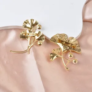 Detailansicht von zwei goldenen Ginkgoblatt-Broschen aus Edelstahl mit Perlen.