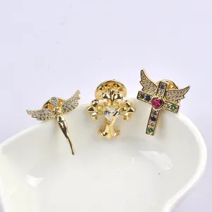 Detailed view of three gold-tone mini cross and angel brooches on a white dish