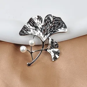 Nahaufnahme einer silbernen Ginkgoblatt-Brosche mit zwei eleganten weißen Perlen
