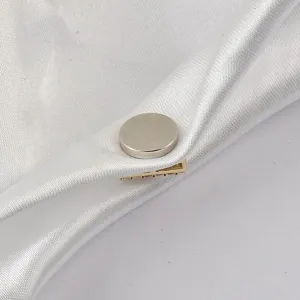 Macro detail of magnetic brooch with gold base and rhinestones on white satin fabric.