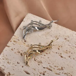 Vue détaillée de broches vagues en argent et or avec strass sur pierre texturée