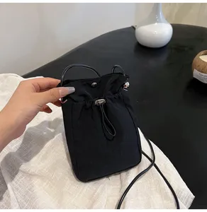 Detalle de un mini bolso bandolera de lona negra con cordón ajustable para mujer.