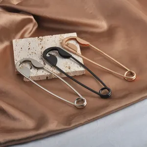 Detailaufnahme von übergroßen dekorativen Sicherheitsnadeln in Gold, Silber, Schwarz.