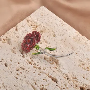 Close-up of elegant red enamel carnation flower brooch pin on a stone background