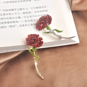 Elegant red enamel carnation brooches showcased on book pages and soft satin fabric.