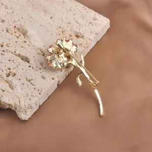 Back view of an elegant golden carnation flower brooch displayed on a textured stone block.