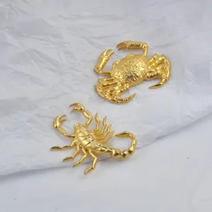 Détail de broches crabe et scorpion dorées de style punk sur fond de papier froissé blanc