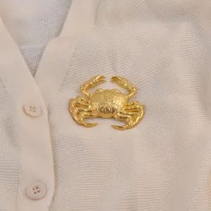 Gros plan d'une broche crabe dorée épinglée sur un cardigan en maille crème
