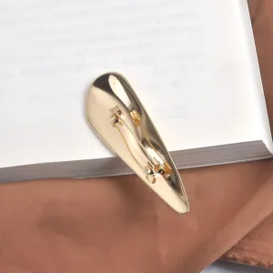 Broche métallique irrégulière dorée élégante présentée sur un fond de livre minimaliste