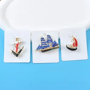 Detailed view of three enamel marine themed brooches with anchor and sailboat designs