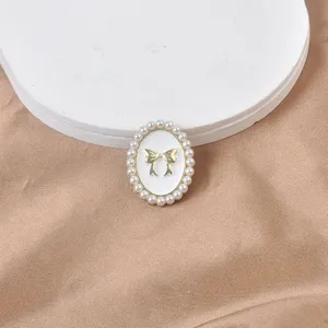 Primer plano de broche magnético ovalado con borde de perlas y lazo dorado.