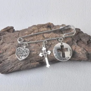 Detailaufnahme der Vintage-Brosche in Silber mit Kreuz- und Herzanhängern auf rustikalem Holz