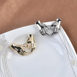 Vista detallada de broches creativos con forma de manos formando un corazón, en oro y plata