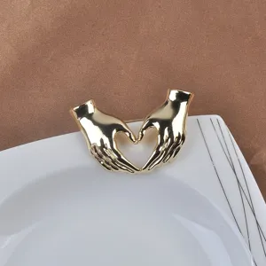 Primer plano de un broche dorado con forma de manos de corazón sobre un plato blanco.
