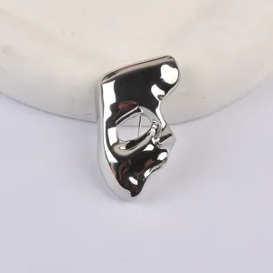 Detailed macro view of a minimalist silver Phantom mask brooch with a glossy finish.
