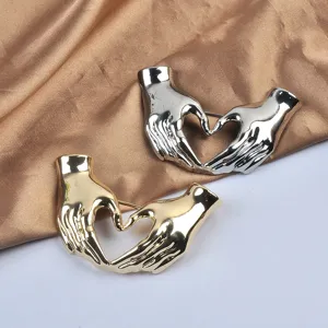 Detailansicht großer silberner und goldener Hand-Herz-Geste Broschen auf Seide.