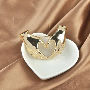 Nahaufnahme einer goldenen Herz-Hand-Geste Brosche in einer Herz-Keramikschale.