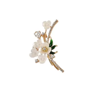 Gedetailleerde close-up van een gouden speld met witte bloemen en sprankelende kristallen