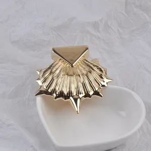Vue détaillée d'une broche coquillage dorée avec un design triangulaire sur un bol cœur