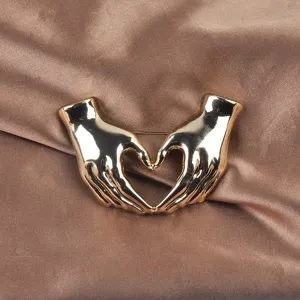 Detailaufnahme einer polierten goldenen Brosche in Form einer Herz-Handgeste