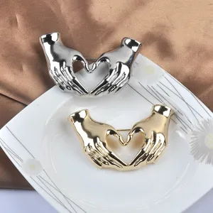 Detailansicht der herzförmigen Brosche in Gold und Silber, die Hände darstellt