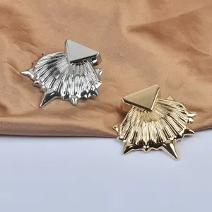 Vue détaillée de broches métalliques en forme de coquillage avec accents triangulaires or et argent.