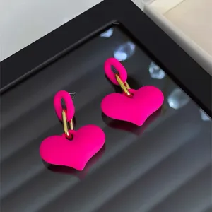 Nahaufnahme von leuchtend rosa herzförmigen Ohrringen mit mattem Finish und Goldgliedern