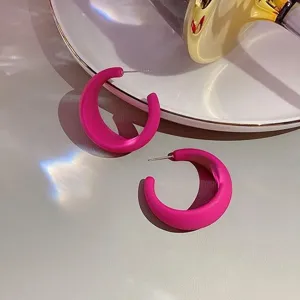 Detailaufnahme von matten C-förmigen Creolen in Pink auf einem weißen Teller.