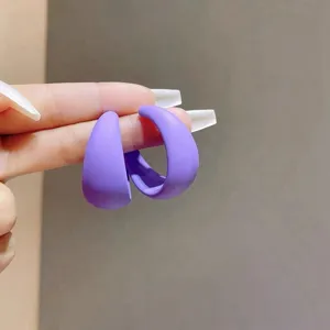 Detailansicht von matten violetten Creolen in Bonbonfarben, von Fingern gehalten