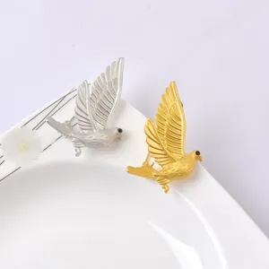 Detailed view of matte gold and silver peace dove bird brooches on a white plate