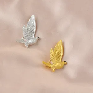 Detailed view of flying peace dove brooches in gold and silver matte finishings