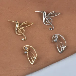 Detailansicht der goldenen und silbernen Kolibri-Broschen mit Notenschlüssel-Design