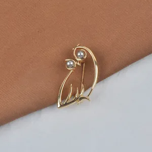 Detailansicht einer eleganten goldenen Vogelbrosche mit zwei grauen Perlenakzenten