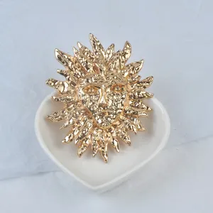 Détail macro d'une broche masque solaire vintage en métal doré effet lave sur un plat blanc