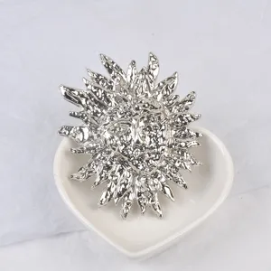 Vue détaillée d'une broche masque de soleil en argent avec texture lave dans un plat cœur.