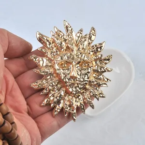 Broche visage soleil en métal doré texturé style vintage tenue à la main pour échelle
