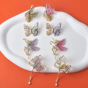 Elegante Kristall-Schmetterlings- und Bienenbroschen auf weißem Tablett vor orangefarbenem Grund