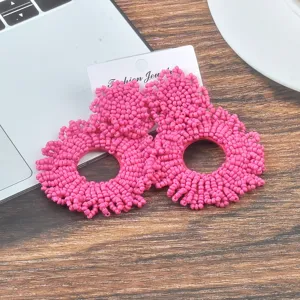 Nahaufnahme von lebhaften rosa handgefertigten Perlenohrringen auf Holzgrundlage.
