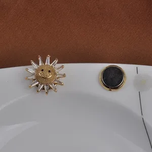 Gedetailleerd beeld van een zonnevormige magnetische broche met lachend gezicht en kristallen.