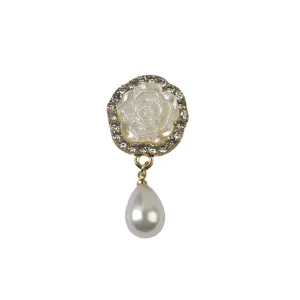 Gedetailleerde opname van een witte roos magneetbroche met strass en parelhanger.