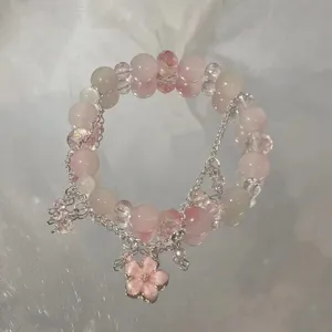 Close-up detail of the pink beaded bracelet with silver chains and a sweet flower pendant.