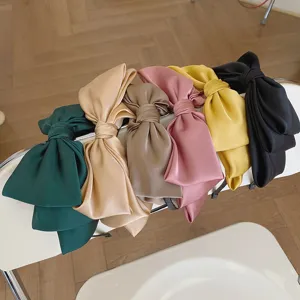 Variety of colorful oversized satin bow headbands displayed on a modern white chair