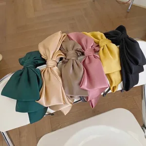 Set of elegant oversized satin bow headbands in multiple colors displayed on a white chair