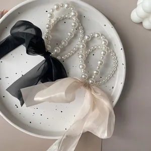 Close-up of elegant pearl hair ties featuring black and beige organza ribbon bows.