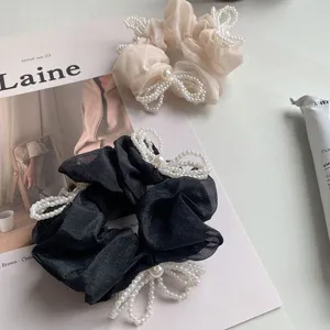 Close-up of elegant black and beige organza scrunchies with pearl bow details.