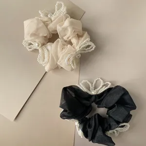 Detailed view of cream and black organza scrunchies with pearl bow decorations.