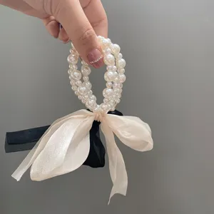 Detailed close-up of a multi-strand pearl hair tie with elegant cream and black ribbon bow.