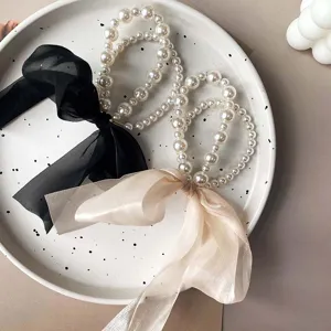 Elegant Korean style pearl hair scrunchies with long ribbon bows on a white plate