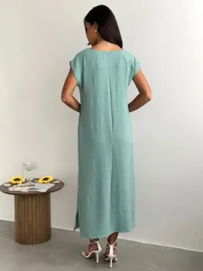 Detail view of a green sleeveless midi dress featuring a back slit and textured fabric.