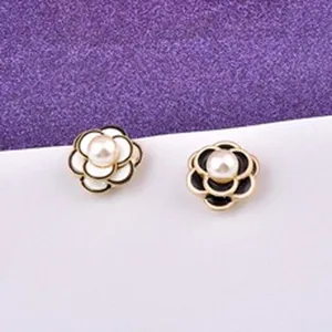 Dettaglio di spille magnetiche a camelia con smalto bianco e nero e perle eleganti